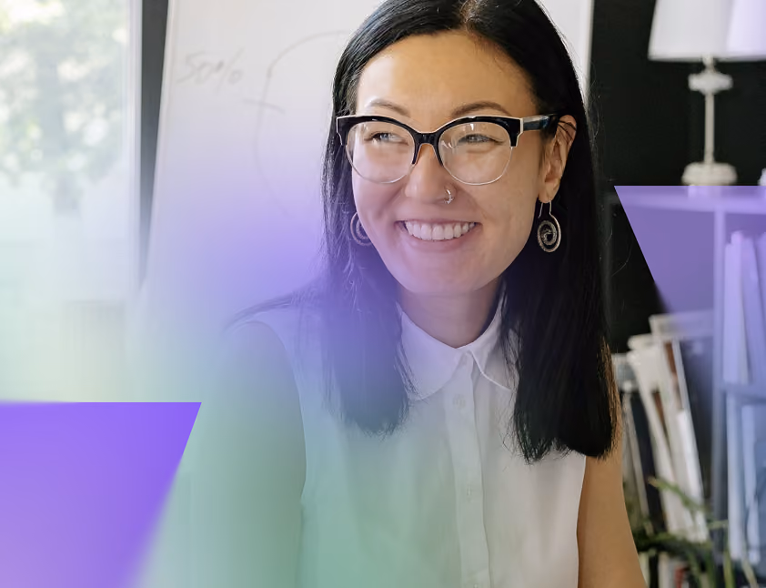 Smiling woman with glasses and black hair wearing a sleeveless white blouse, in an office setting.