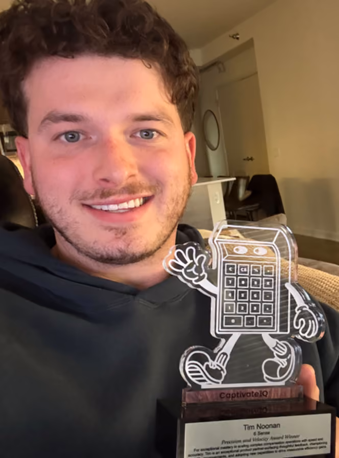 Smiling man holding a trophy with a walking calculator figure on top and an award plaque below.