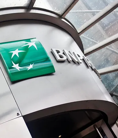 BNP Paribas logo on a curved metallic building exterior under a glass roof with raindrops.