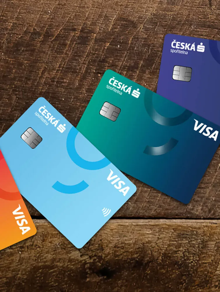 Four Česká spořitelna Visa credit cards in orange, light blue, teal, and purple arranged on a wooden surface.