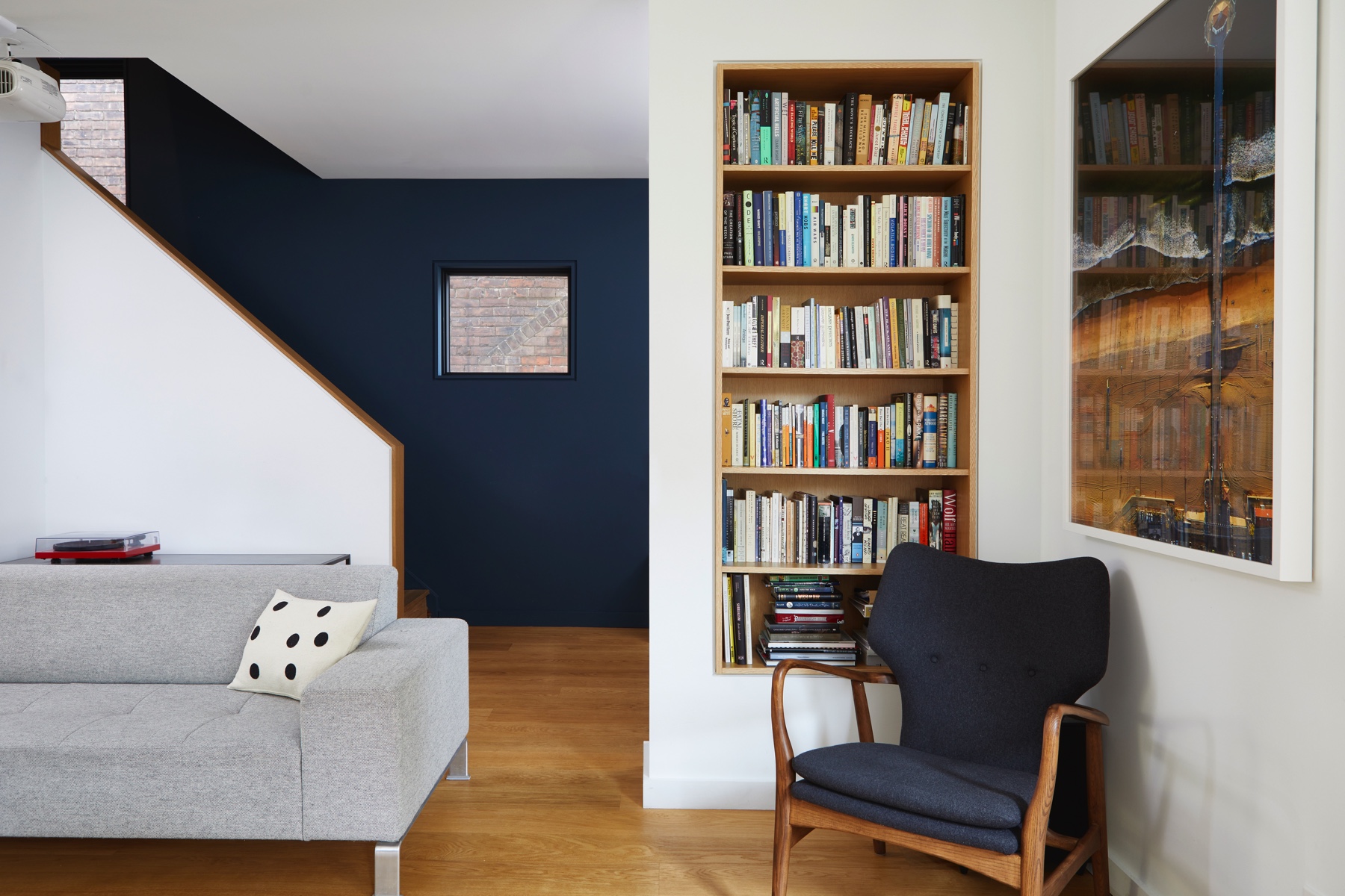 Trinity Bellwoods Treasure: In the living room, a deep navy accent wall and built-in oak bookshelf give the space some drama, while a bay window dining nook framed in black steel brings in light from the street