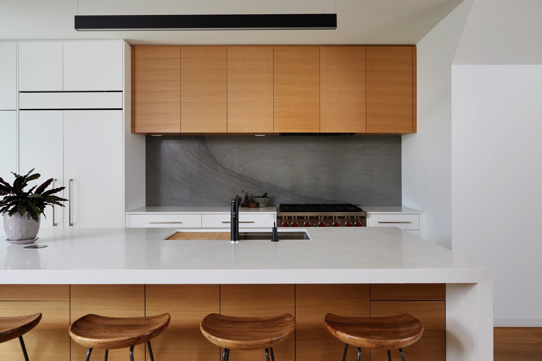 Trinity Bellwoods Treasure: The kitchen pairs crisp white flat-panel cabinetry with a warm oak waterfall island and matching upper cabinets, set against a honed stone backsplash and wide-plank oak floors