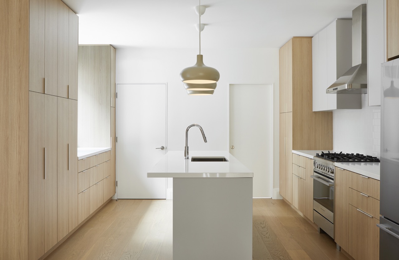 Annex Duplex: Waterfall quartz islands anchor each space, paired with full-height oak pantry walls, integrated stainless appliances, and a white subway tile backsplash