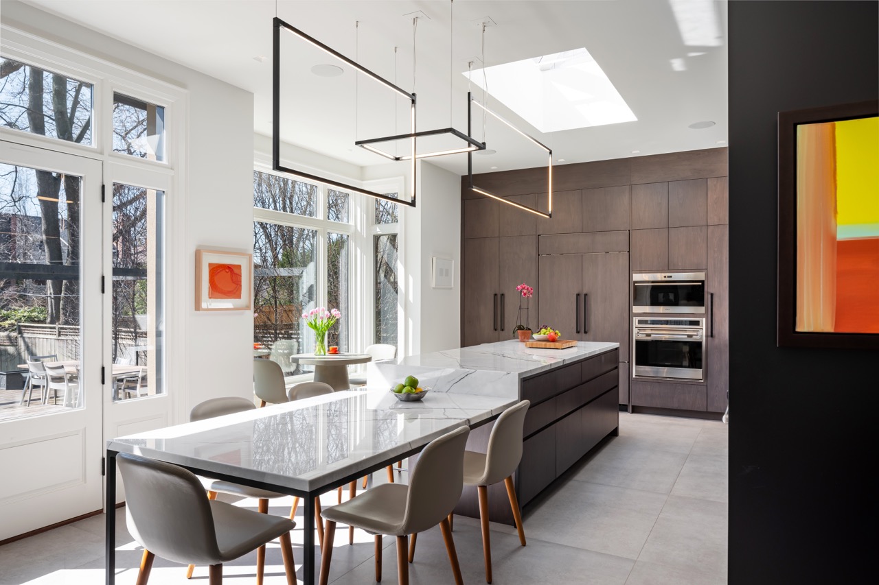 Stylish South Hill: This South Hill renovation is anchored by a dramatic kitchen that doubles as the dining room: a single waterfall marble island runs the length of the space, seating both stools and a full dining table beneath a run of skylights…