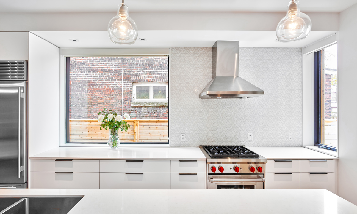Roncesvalles Reno: A clean white kitchen with a subtle geometric backsplash is located in the heart of the home, with large windows in the side wall that inject light deep into the middle of the house