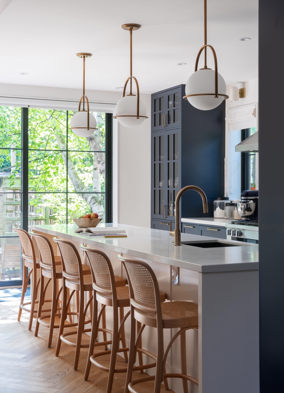Rusholme Restored: The adjoining kitchen goes moody with navy blue cabinetry, brass dome pendants, and a waterfall island with seating for the whole family