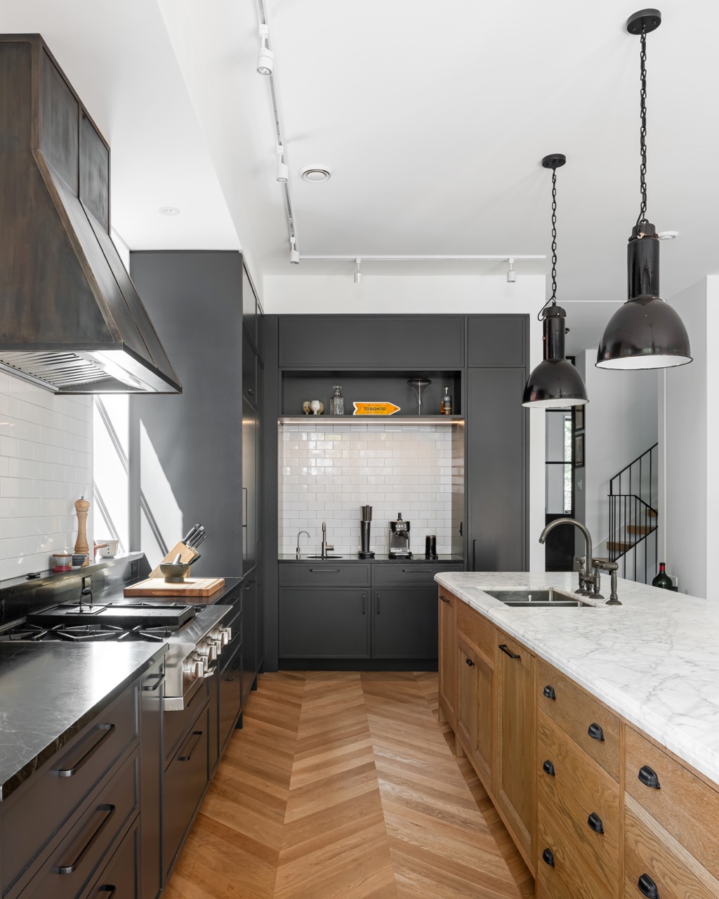 Picturesque Parkside: The exterior kept its dark gabled roofline, wraparound porch, and brick facade intact, while the interior was reimagined around a moody charcoal kitchen with a white oak island, subway tile hood surround, and full-height…