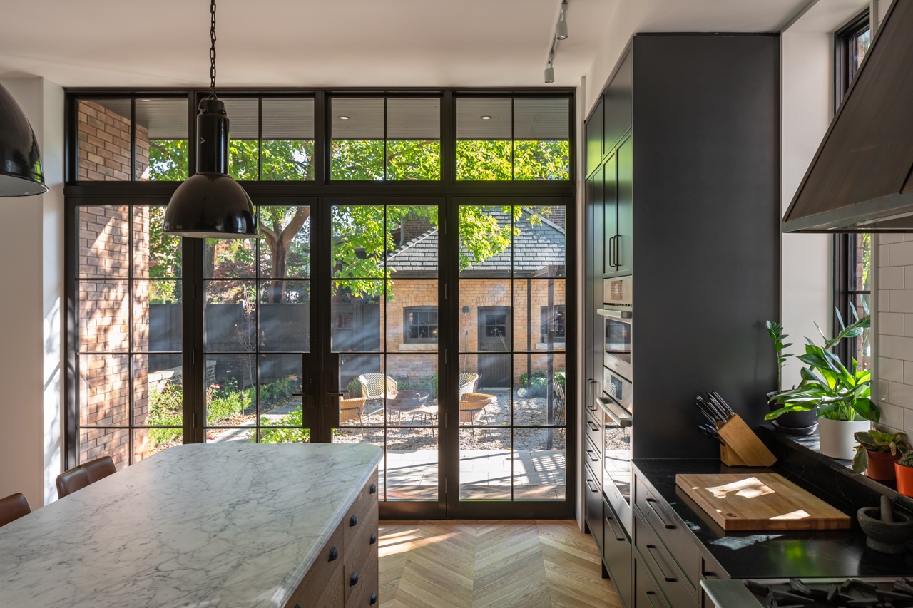 Picturesque Parkside: The exterior kept its dark gabled roofline, wraparound porch, and brick facade intact, while the interior was reimagined around a moody charcoal kitchen with a white oak island, subway tile hood surround, and full-height…