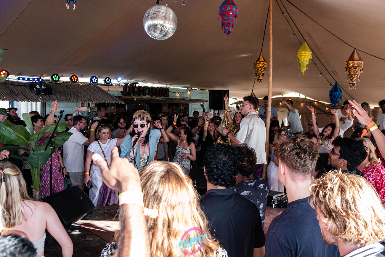 Crowd enjoying a live music performance under a tent decorated with colorful lanterns and a disco ball.
