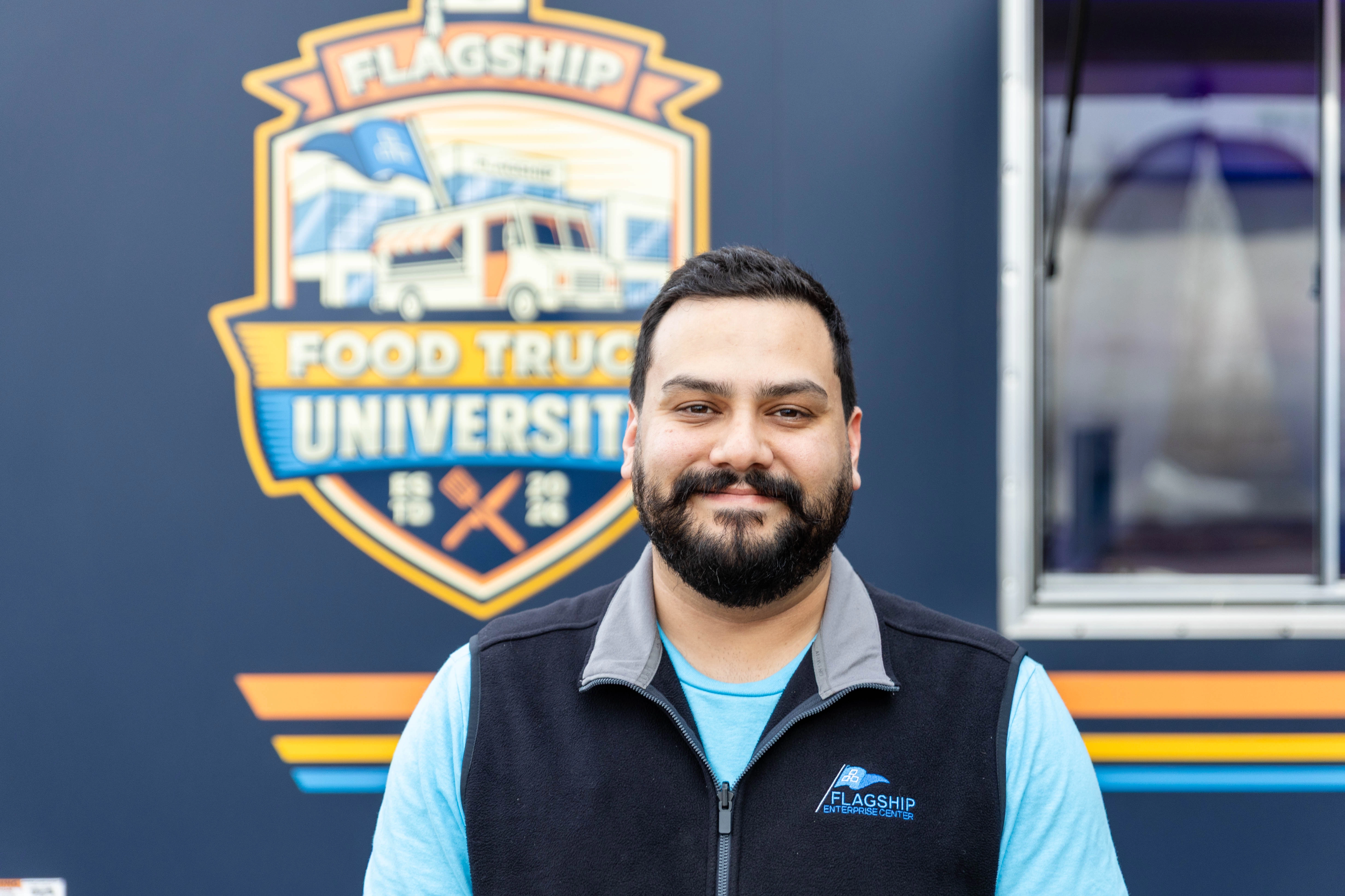 Josh Zacchaeus, Director of Venture Development, stands in front of the Flagship Food Truck University branded food truck.