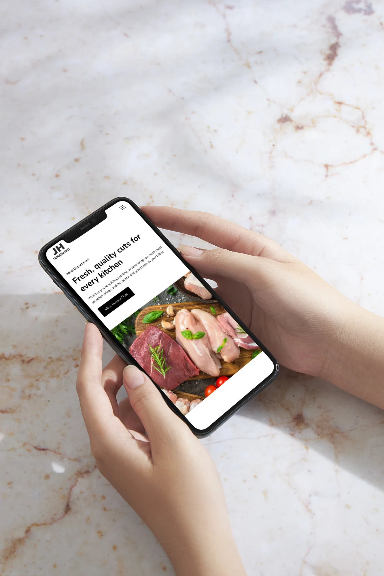 Hands holding a smartphone displaying JH Supermarket's meat department webpage featuring fresh cuts of meat including raw beef and chicken breast with herbs on a wooden board.