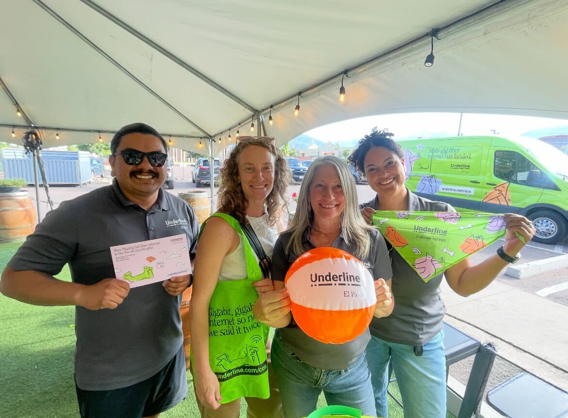 Four people smiling under a tent holding Underline branded items including a card, ball, and bandana.