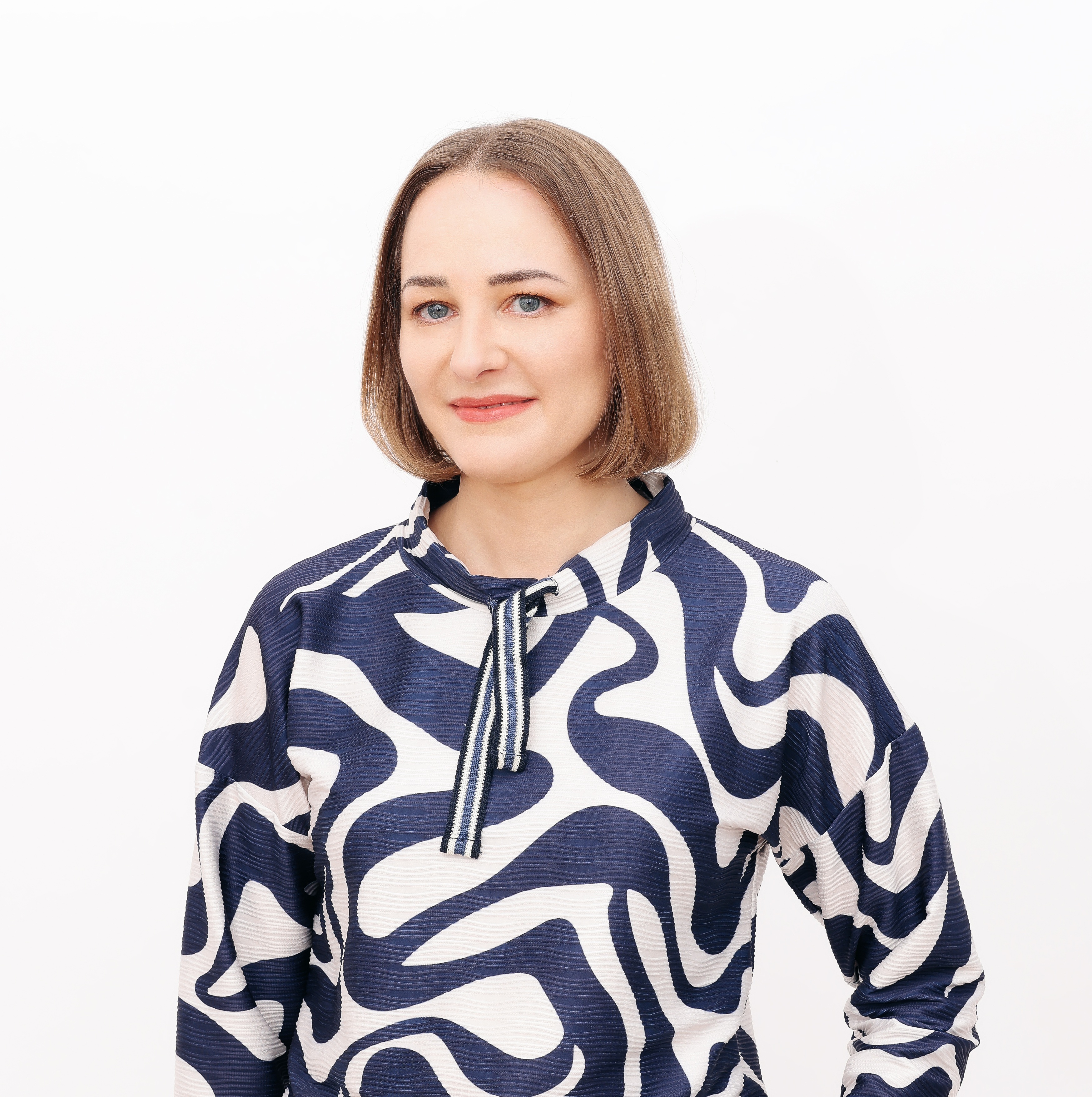 Na zdjęciu widać młodą kobietę, wykadrowaną do pasa, w biało - grantowej bluzce.