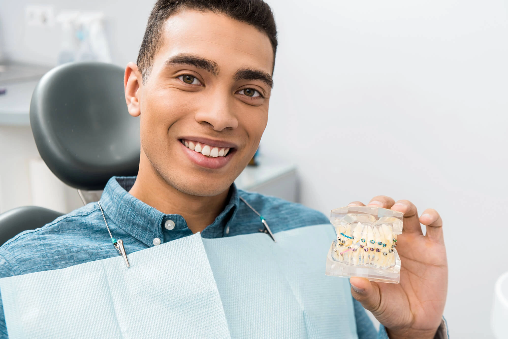 man smiling and holding teeth model with affordable braces
