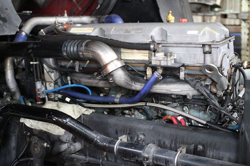 Close-up of a diesel truck engine with exposed piping, wiring, and hoses during maintenance inside a repair facility or workshop.
