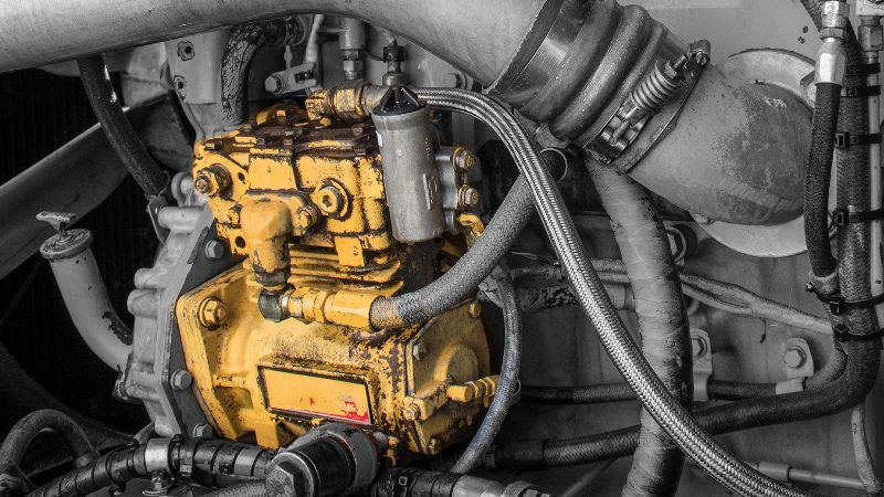 Close-up of a yellow diesel truck air compressor surrounded by hoses, pipes, and fittings inside the engine compartment, highlighting detail.