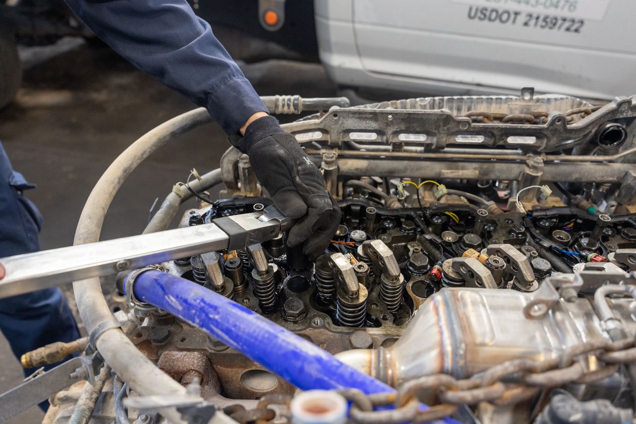 Mechanic wearing gloves uses a torque wrench to adjust valve components on a diesel engine during detailed repair inside workshop.