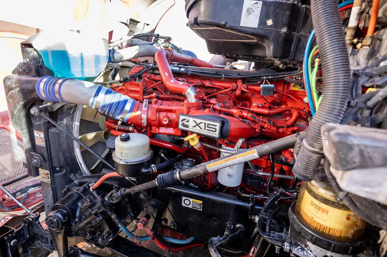Cummins ECM tuning on a red X15 engine with wiring, hoses, and filters visible.
