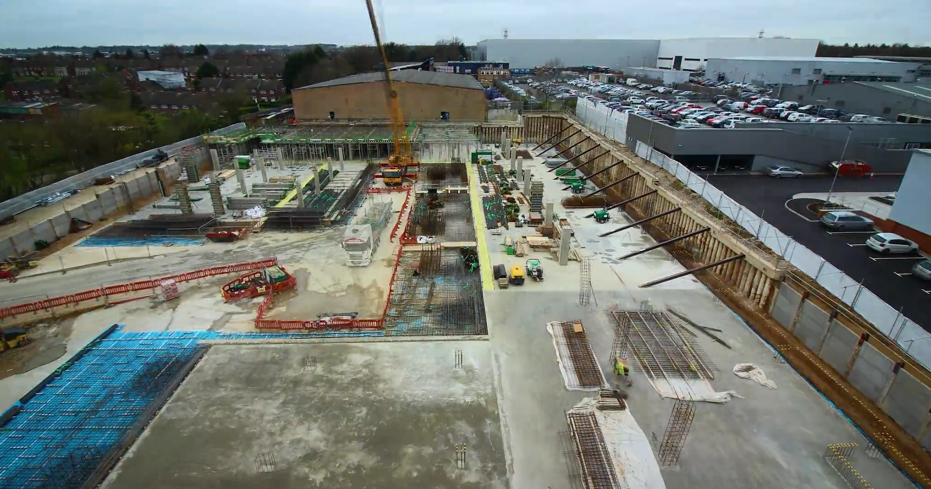 A large construction site with concrete foundation, rebar, machinery, and surrounding retaining walls.