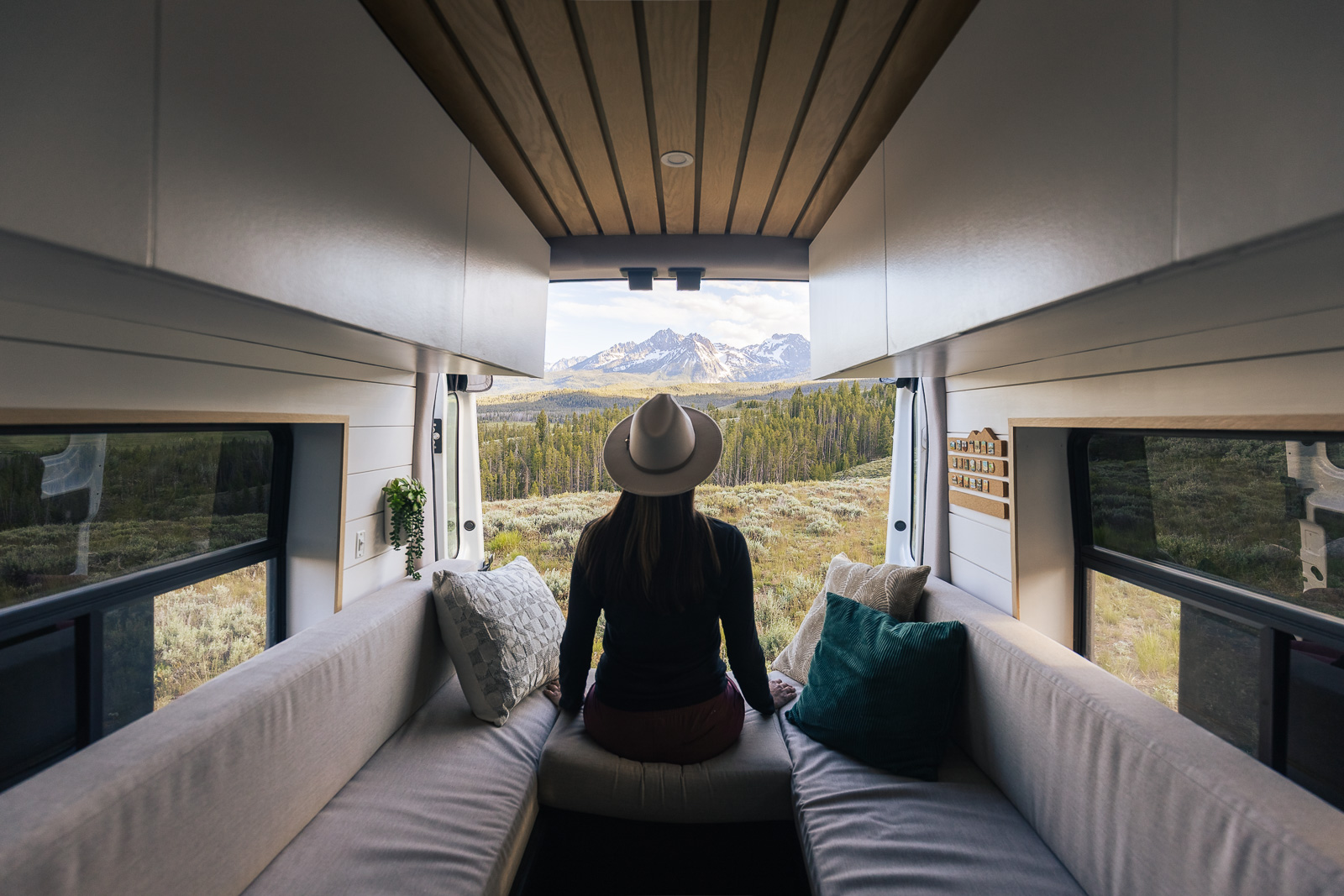 A woman sitting in the back of a campervan with the rear doors open to a scenic view of the Sawtooth Mountains in Idaho.