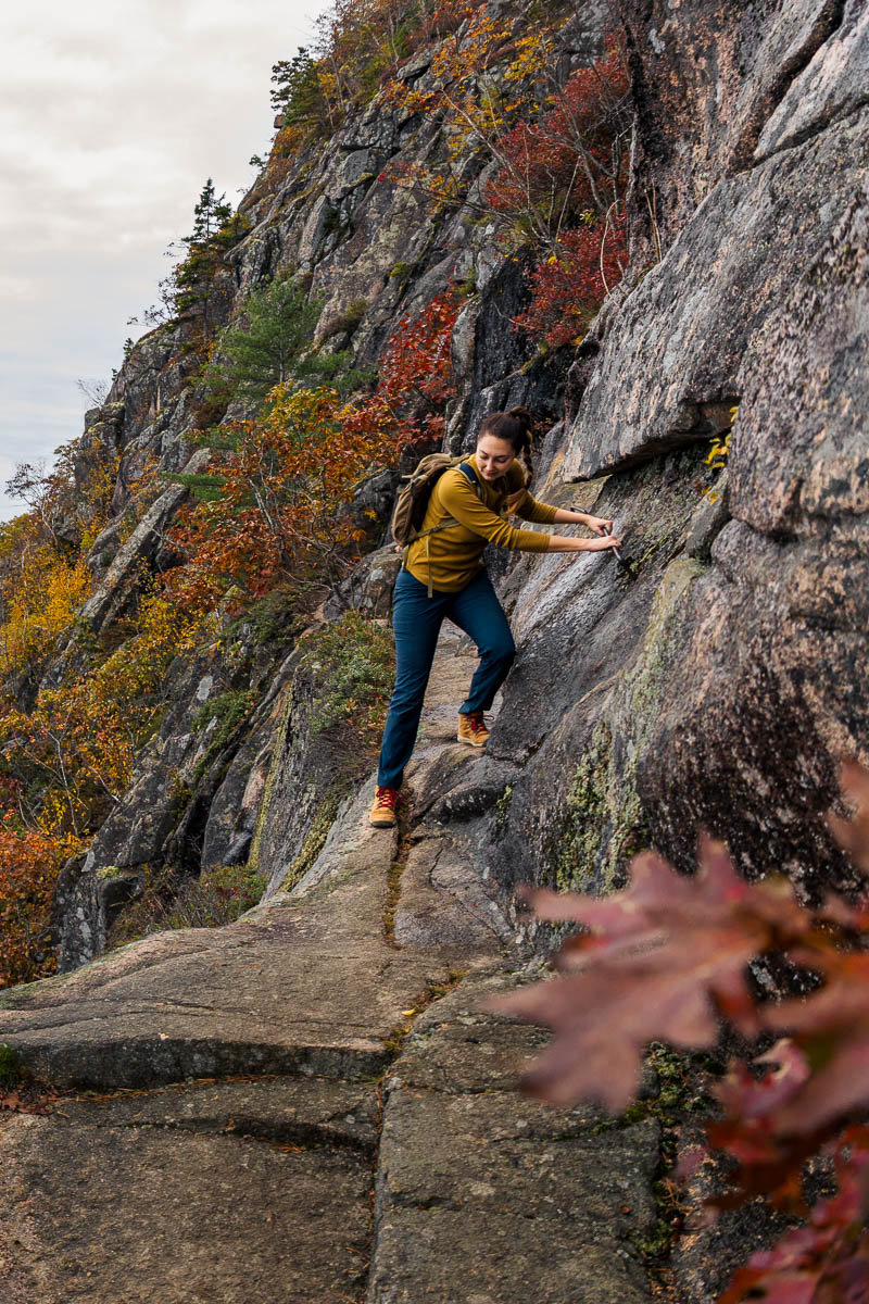 A woman holds onto a rock face while hiking the Precipice Trail in Acadia National Park