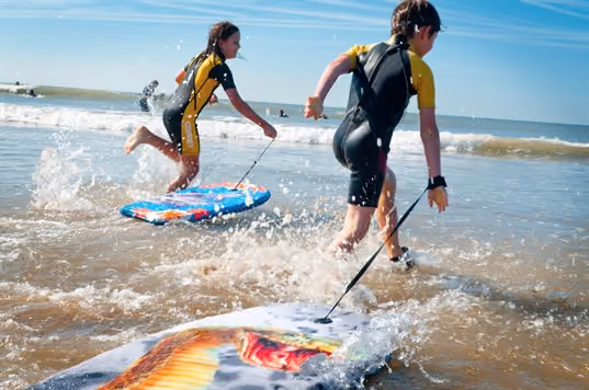 Two children running into the sea with body boards