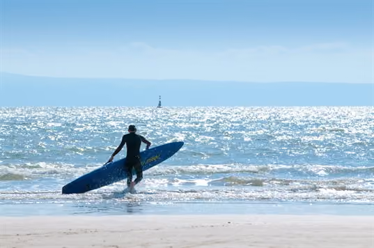 Surfer walking in the shallow sea with board in hand