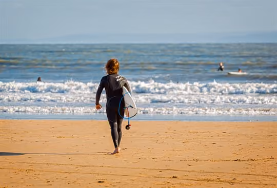 Surfer in wet suit walking towards sea with board in hand