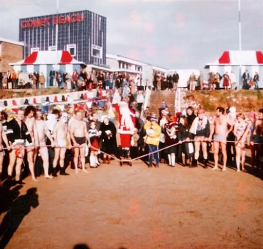 Aged photograph of a line up of swimmers ready to run into the sea on Christmas Day