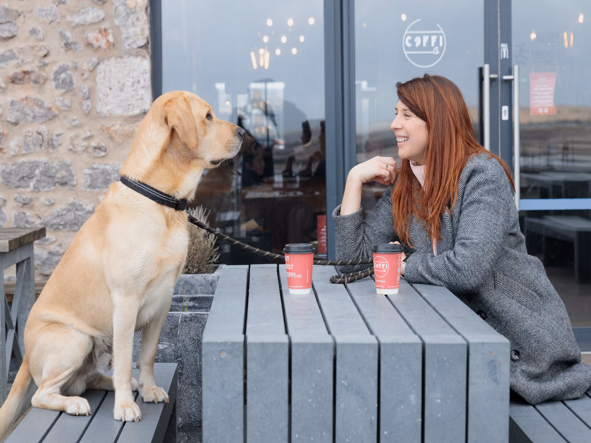 Dog and owner sitting at a bench having a coffee