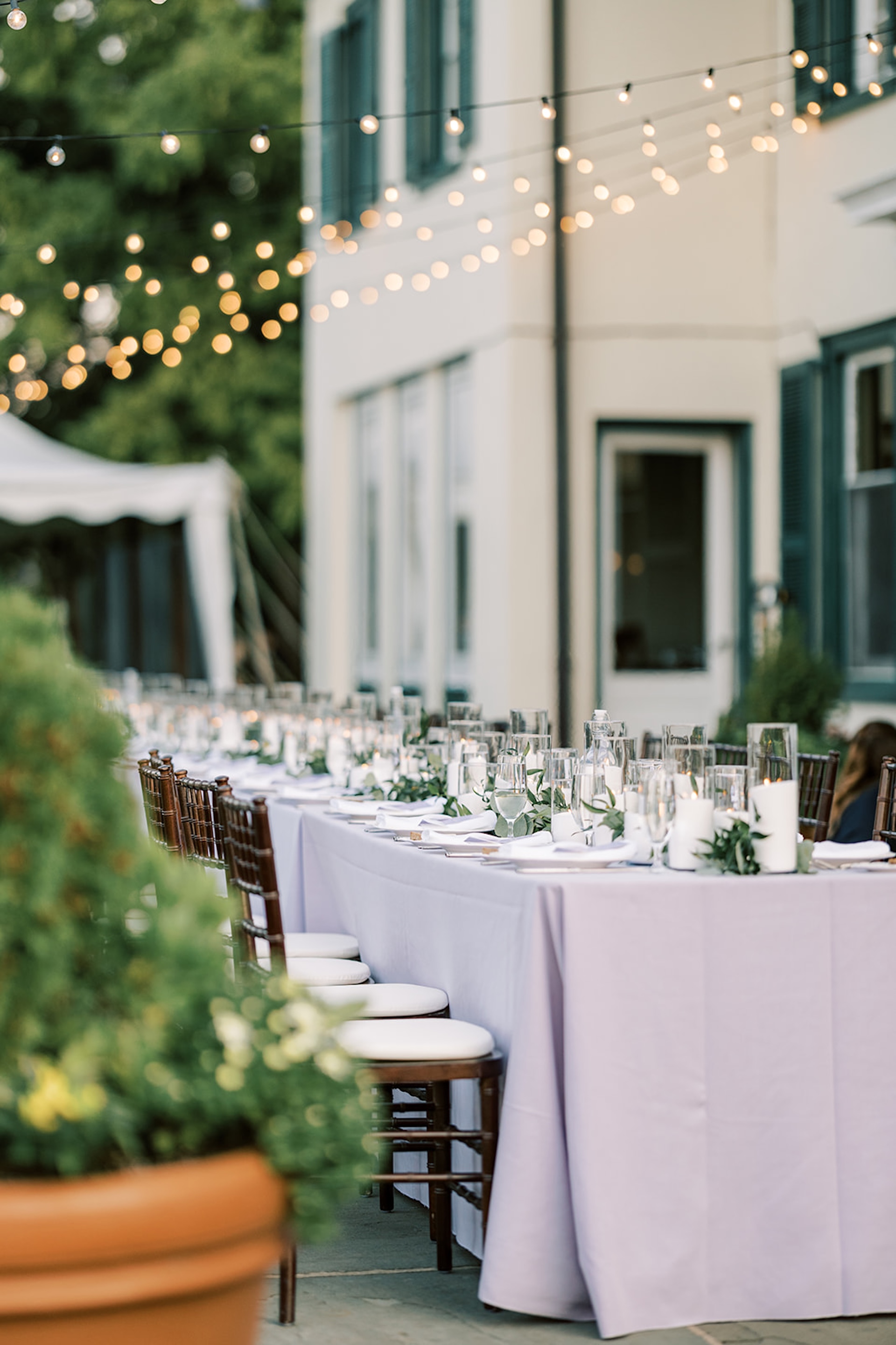 Pretty long table for al fresco dining, lavender cloths give a pop of color, and market lighting adds ambience.