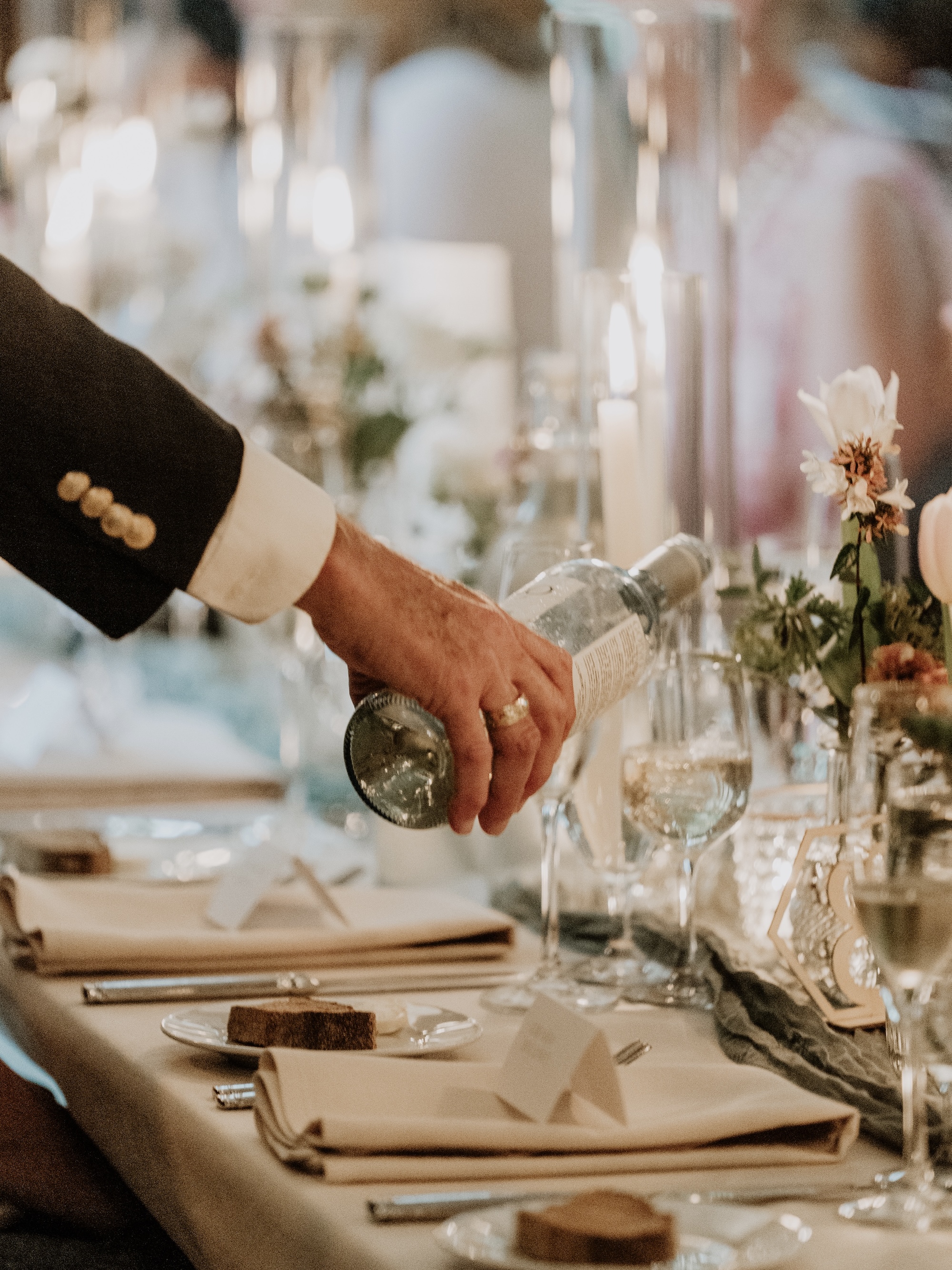 A head waiter pours champagne at a wedding reception table during dinner at a Peachtree Weddings celebration.