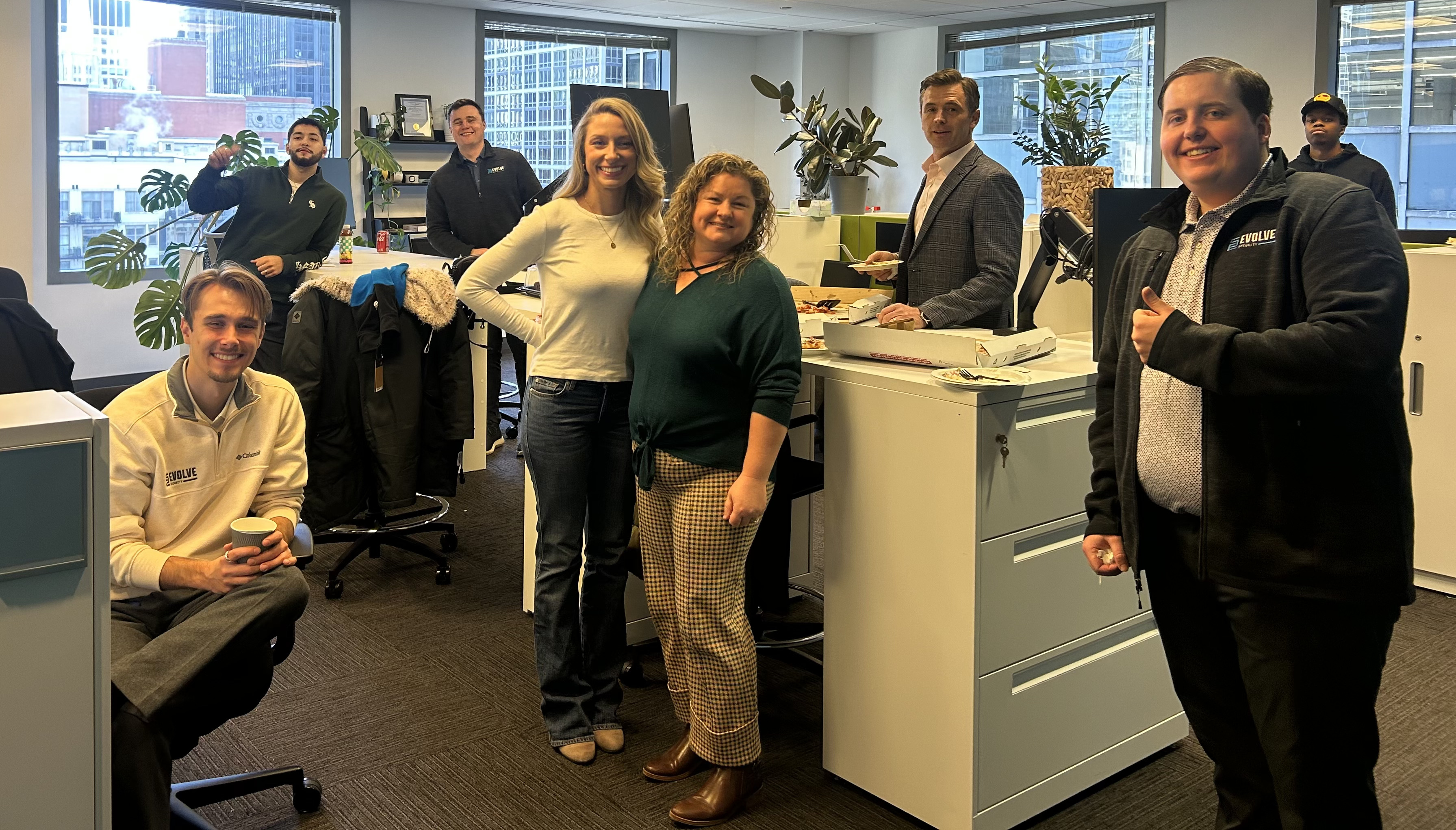 Five diverse colleagues gathered around laptops, engaged in a collaborative discussion in a bright office space.