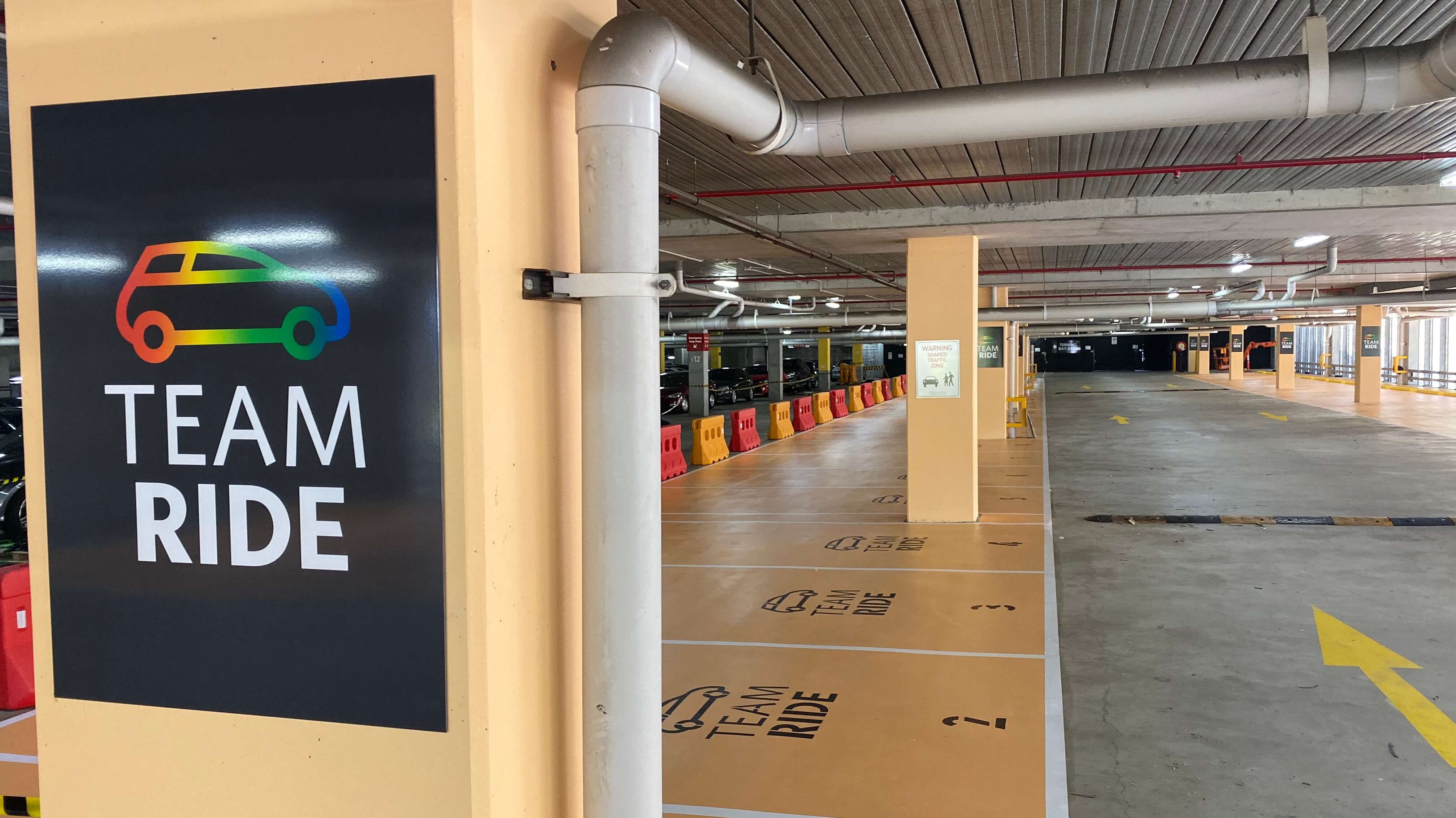 Indoor parking area with marked 'Team Ride' carpool spaces and a colorful car icon sign.