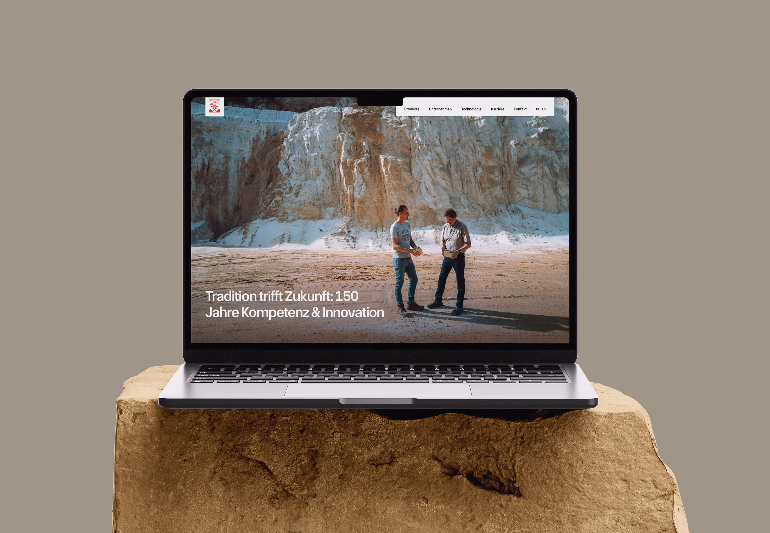 Ein MacBook Mockup auf einem Stein mit beigen Hintergrund zeigt 2 Personen in einer Sandgrube mit dem Text "Tradition trifft Zukunft. 150 Jahre Kompetenz & Innovation."