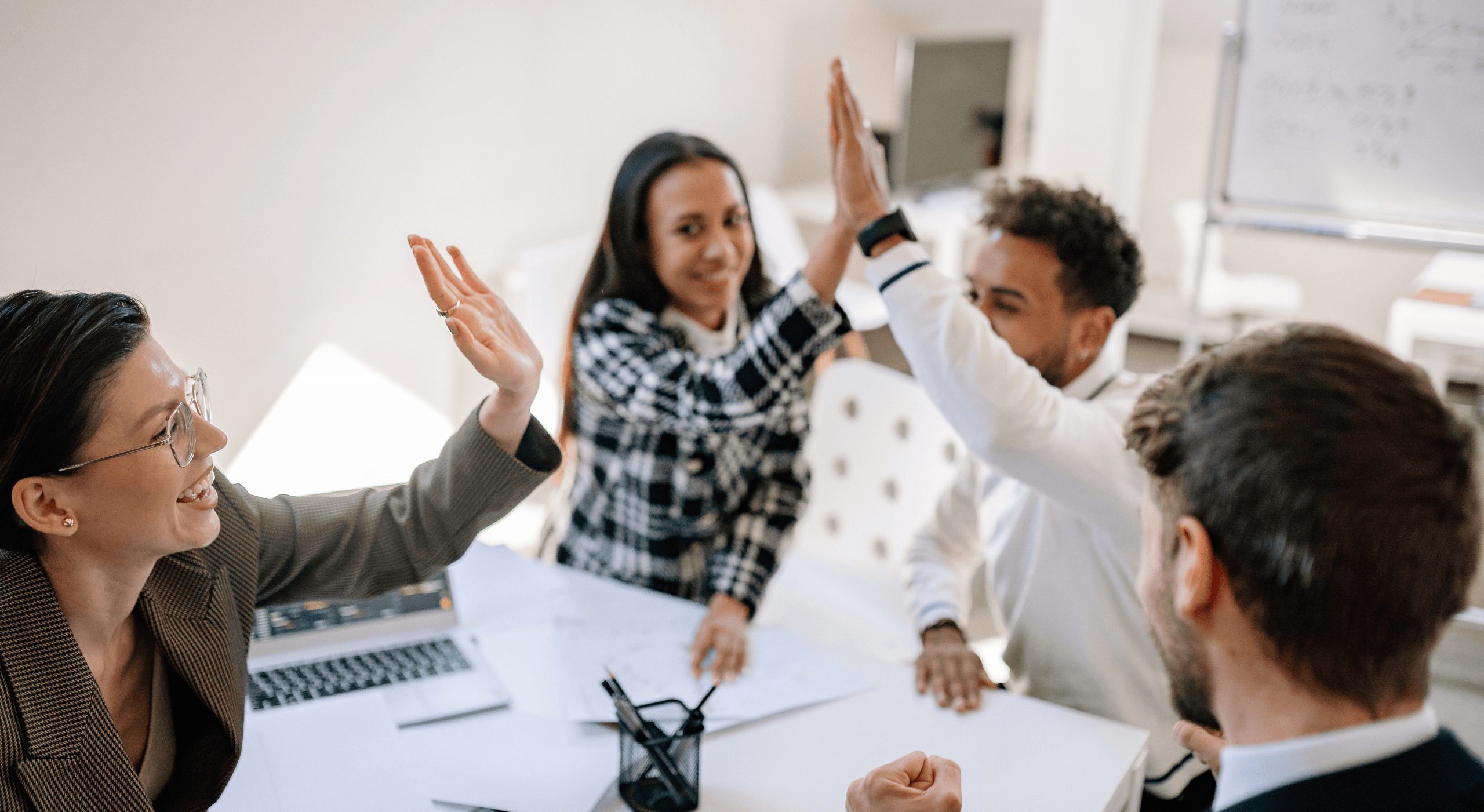 Group of coworkers smiling and high-fiving during a meeting