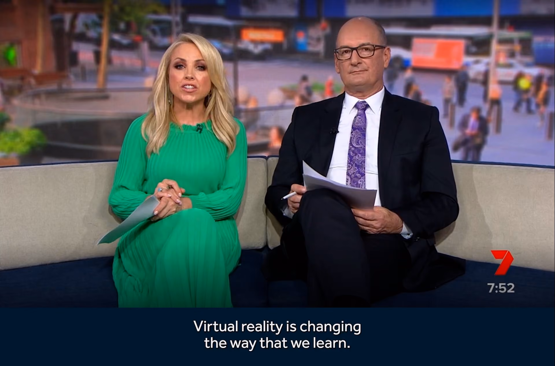 Two news anchors seated on a couch with subtitle about virtual reality and learning on screen.