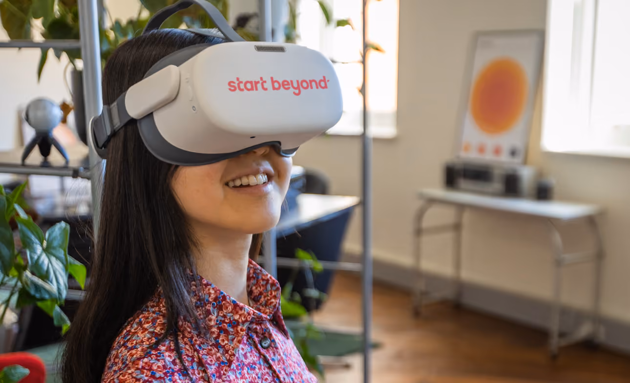 A smiling woman wears a VR headset in an office space completing solo learner mode.
