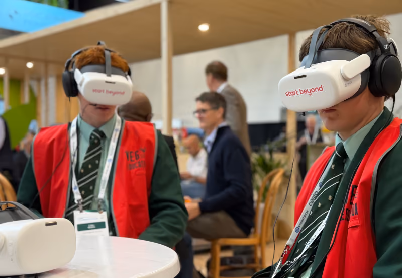Two students in school uniforms wear "start beyond" VR headsets with headphones at an expo booth.