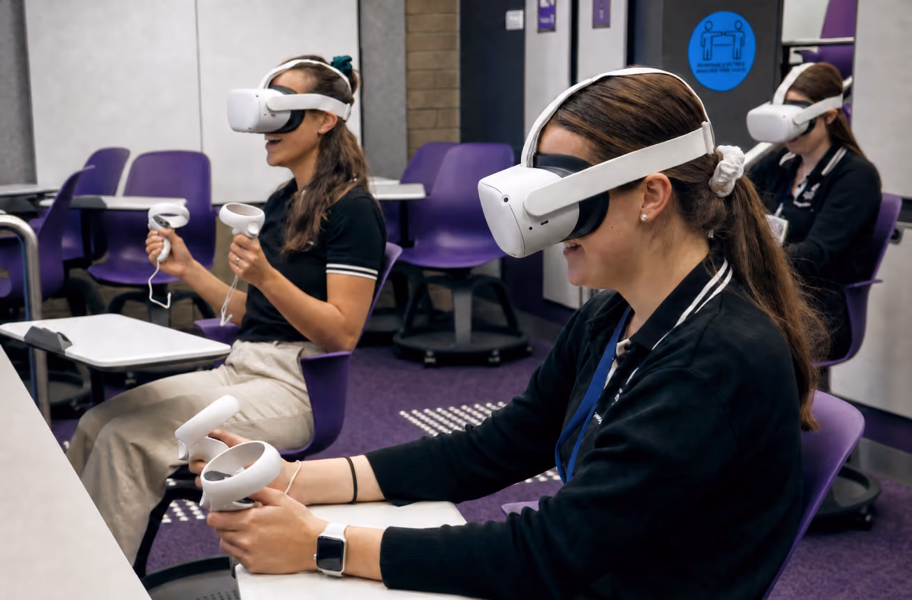 Trainees sit at desks in a classroom, wearing VR headsets and holding controllers during a training exercise.