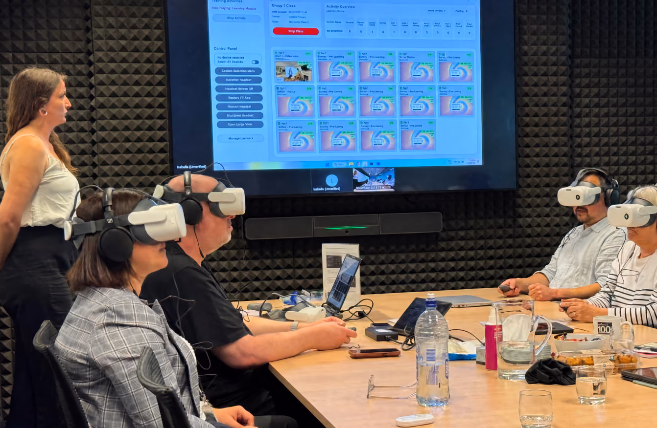A trainer leading a group of trainees wearing VR headsets while a large screen shows the class control dashboard monitoring each learner's progress.