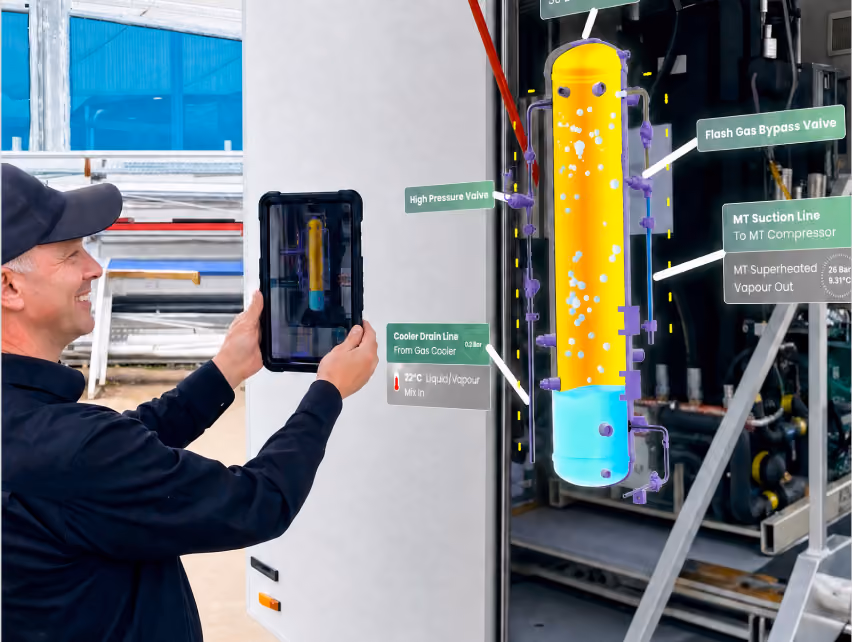 A man smiles while holding a tablet that shows an AR overlay of a receiver vessel, labeled with the High Pressure Valve, Flash Gas Bypass Valve, MT Suction Line, and Cooler Drain Line.