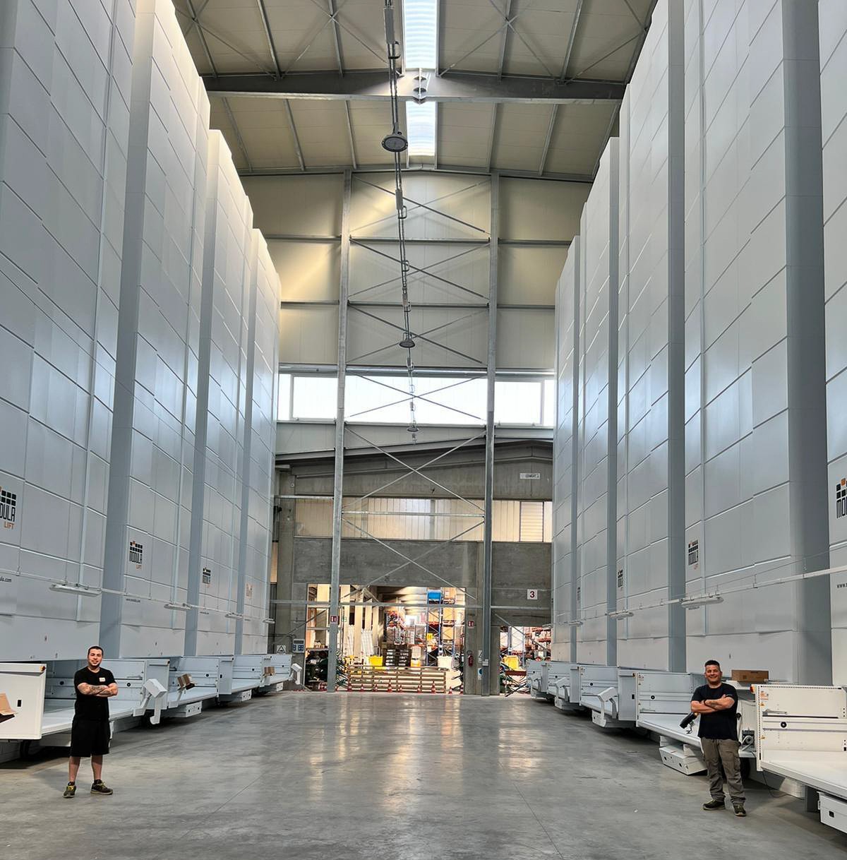 Two individuals standing in front of 9 Modula Lifts that reach the warehouse ceiling.