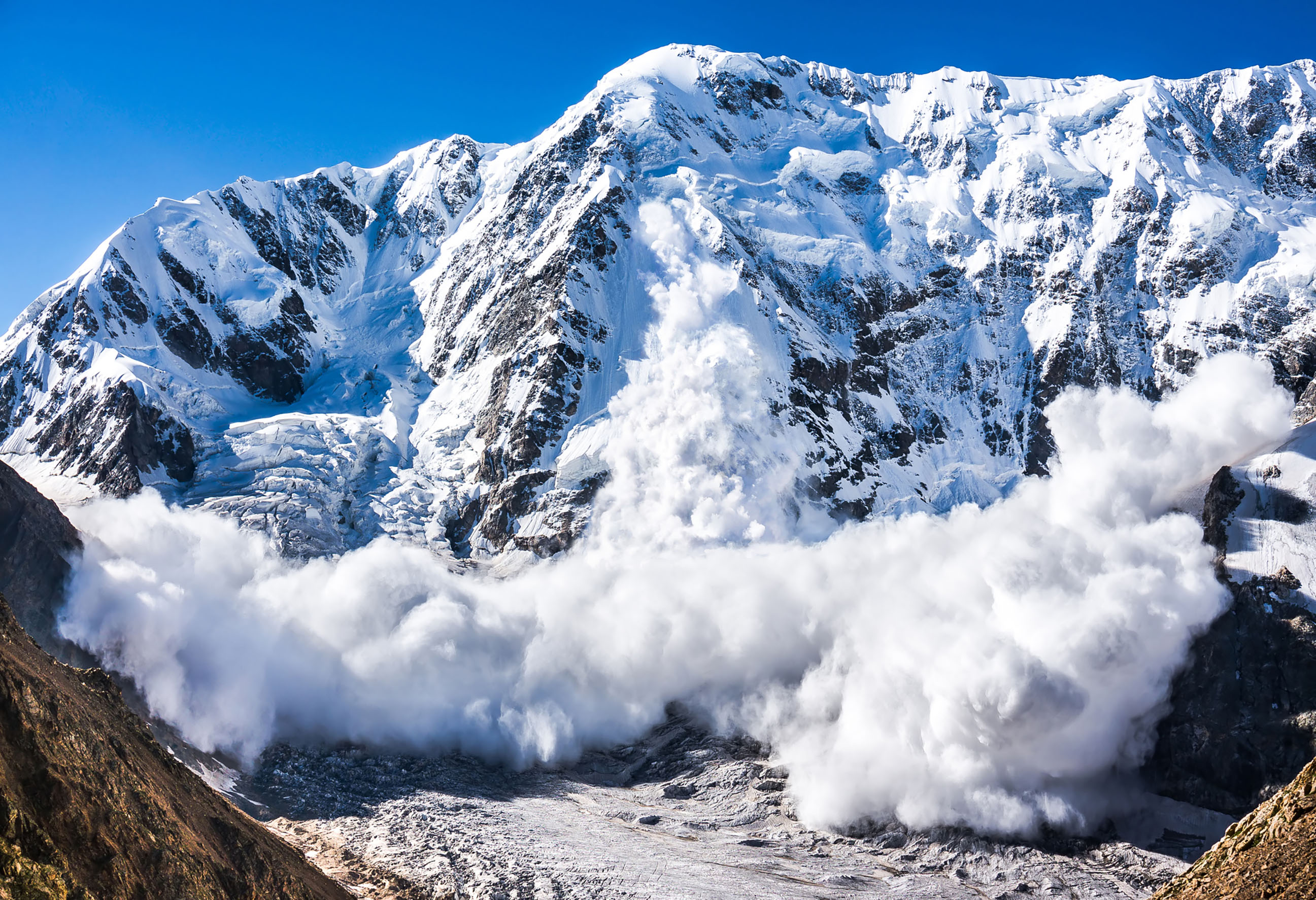 An avalanche of white snow descents from a central point on the mountain face in the center of the image. Avalanches can be controlled and prevented just like PR crises.