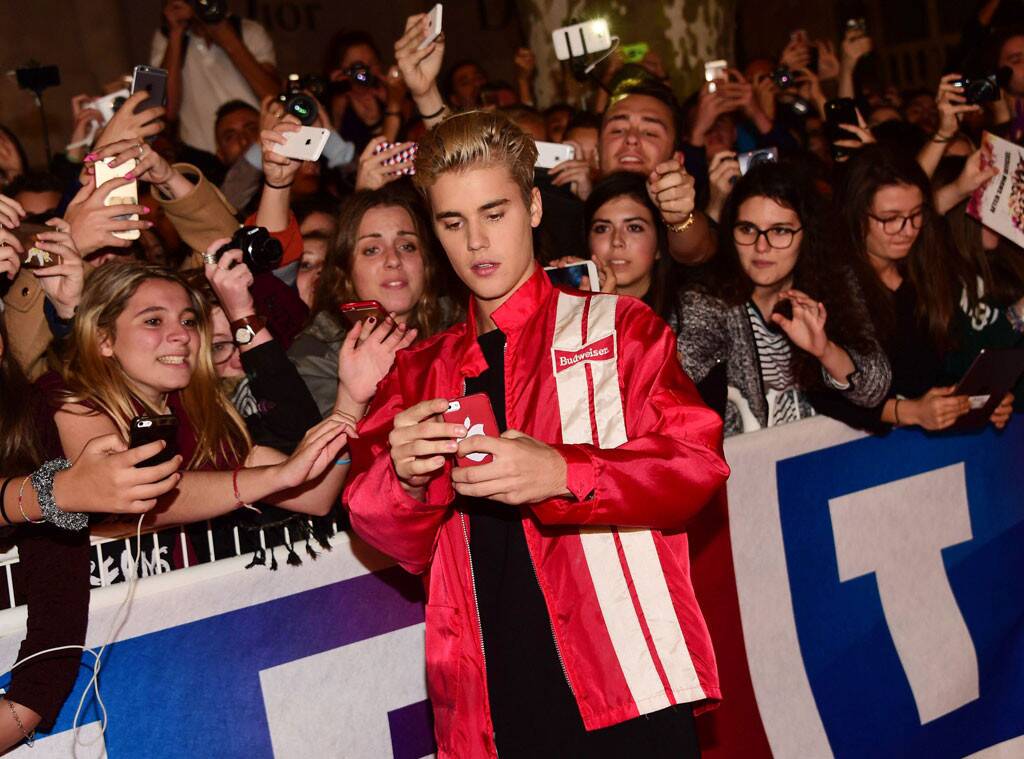 Justin is taking a picture with several fans. Many of the fans are holding up their phones to get a picture of him. Giving his customers/ fans an excellent experience was his goal.