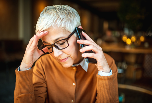 A older business woman, with short white hair, holds her hand up to her forehead as she takes a call. Her eyes are shut and she looks disappointed with the news she's receiving. Now, she's got to figure out how to reduce churn after this bad customer experience. 
