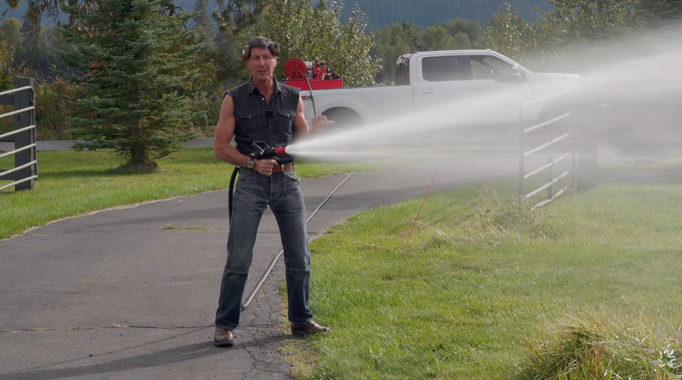 Wranglerstar spraying water from the VIPER Nozzle on his property, with the 125HP-equipped pickup parked behind him