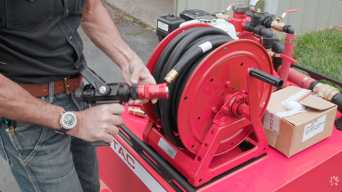 Close-up of the red VIPER Nozzle with a black pistol-grip bale shut-off, held next to the 125HP hose reel
