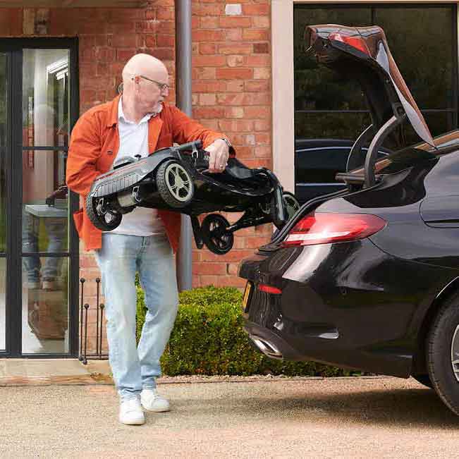 Man tilt een opgevouwen scootmobiel in de kofferbak van een auto.