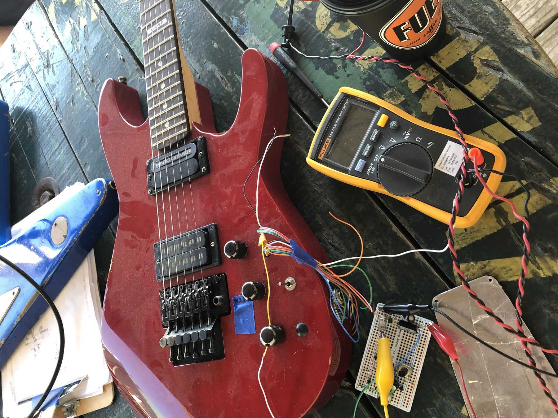 A Hard Driver sustainer prototype under test with a Fluke multimeter on a workbench